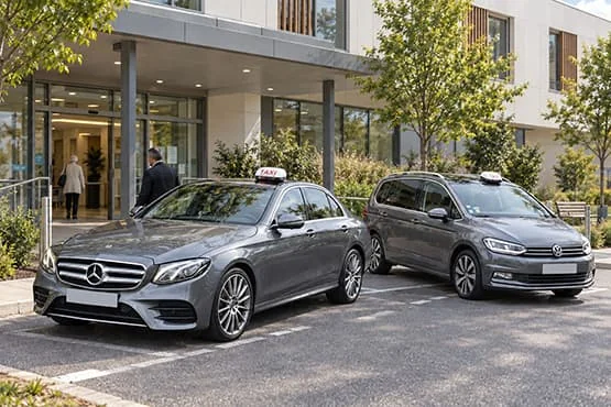 Berline Mercedes grise et monospace Volkswagen gris stationnés devant un bâtiment moderne.